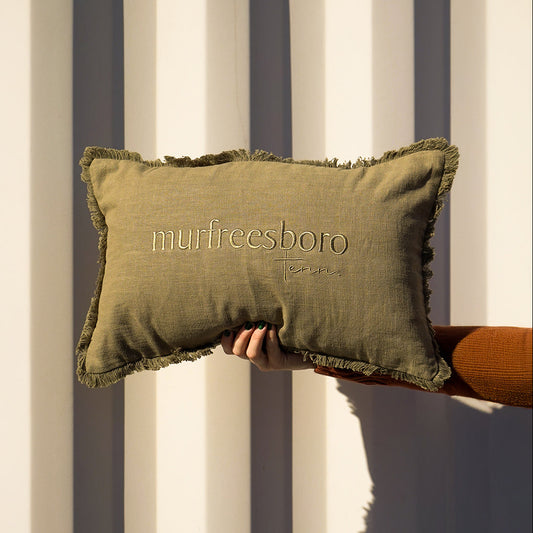 Green pillow with 'murfreesboro' embroidery held against a striped background