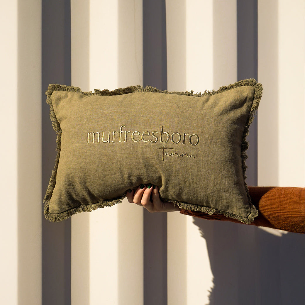 Green pillow with 'murfreesboro' embroidery held against a striped background